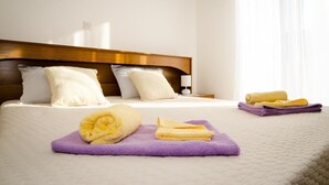 Habitación de hotel con una cama bien hecha, cabecera de madera y una ventana con cortinas translúcidas.