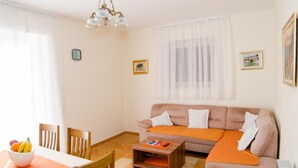 Una sala de estar con sofá, mesa de centro y mesa de comedor. Hay dos cuadros en la pared y una araña.
