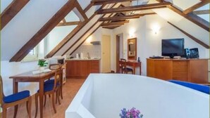 Ein Schlafzimmer im Dachgeschoss mit geneigter Decke, einem großen Fenster, einem eingebauten Schreibtisch und einer weißen Badewanne.