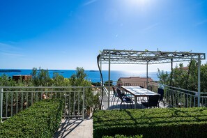 Eine Terrass mit Pergola, einem Tisch mit Stühlen und Blick aufs Meer.