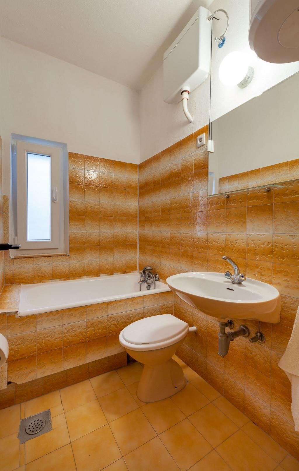 A bathroom with a bathtub, sink, and toilet, featuring orange-tiled walls and a window.