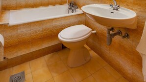 Ein Badezimmer mit Badewanne, Waschbecken und Toilette, mit orangefarben gefliesten Wänden und einem Fenster.