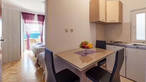 Ein gemütlicher Raum mit Bett, Esstisch und Stühlen, einer kleinen Küchenzeile und Meerblick durch ein Fenster.