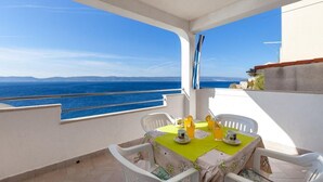 Ein Balkon mit Tisch für zwei Personen, mit Blick auf ein klares, blaues Meer und entfernte Küsten.