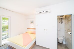 Una camera da letto con un letto, un bagno con il water e la doccia, e una finestra con vista sul verde.