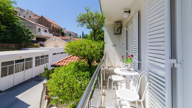 Een balkon met een witte tafel en stoelen, een bloempot en uitzicht op de straat daaronder.