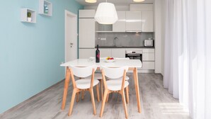 A modern kitchen with white cabinets, a white dining table with four chairs, and a pendant light. - Dva Galeba - Standard One Bedroom Apartment with Terrace (101) (Bol)