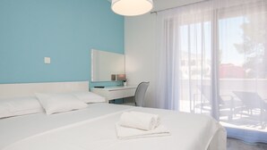 A hotel room with a large bed, a desk, a chair, and a window with a view of outdoor furniture. - Dva Galeba - Standard One Bedroom Apartment with Terrace (101) (Bol)