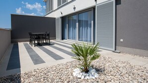 A modern building with a patio area featuring a table and chairs, a palm plant, and a gravel pathway. - Dva Galeba - Standard One Bedroom Apartment with Terrace (101) (Bol)