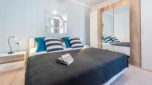 A modern bedroom with a large bed, a bedside table, a mirror, and a wardrobe.