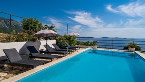 A poolside area with lounge chairs and umbrellas, overlooking a body of water and distant islands.