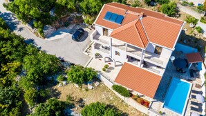 A two-story house with a swimming pool, solar panels, and a car parked in the driveway.
