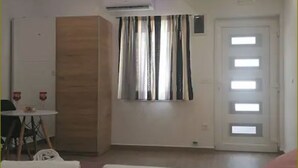 Een hotelkamer met een bed, een kleine tafel met stoel, een houten garderobe, een raam met gordijnen en een deur met meerdere ramen.
