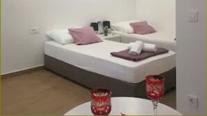 Een kleine, moderne slaapkamer met een enkel bed, een nachtkastje en een tafeltje met twee rode glazen.