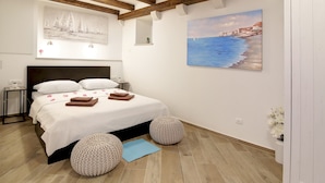 A bedroom with a bed, wooden beams, a painting of a coastal scene, and a small bedside table. - Apartment City Gem - Studio (Dubrovnik)