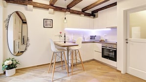 A kitchen with white cabinets, a wooden ceiling, and a dining area with two chairs and a table. - Apartment City Gem - Studio (Dubrovnik)