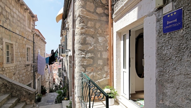 A narrow street with stone buildings, a metal railing, and a sign indicating an apartment. - Apartment City Gem - Studio (Dubrovnik)