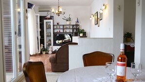 Spiseområde med et bord dækket til to, en sofa og et fjernsyn i baggrunden.