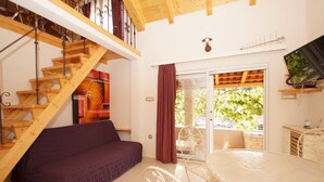 A cozy room with a wooden staircase, a purple sofa, a white table, and a TV on a shelf.