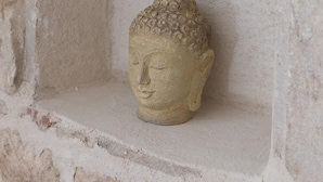 A stone Buddha statue in a recessed alcove with rough stone walls.