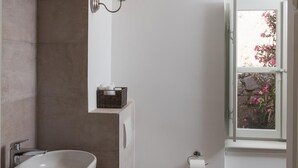 A modern bathroom with a freestanding sink, a toilet, and a window with a view of flowers.
