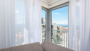 Una sala de estar moderna con un sofá gris, grandes puertas correderas de vidrio y vistas a un paisaje urbano y montañas.