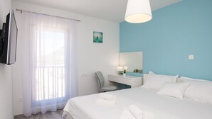 Habitación de hotel con una cama grande, un escritorio, una silla, un televisor y una ventana con cortinas traslúcidas.