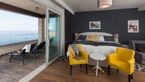 Una habitación de hotel moderna con balcón, una cama con vistas, una mesita y dos sillas amarillas.