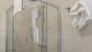 Ducha envuelta en vidrio con cabezal de ducha de mano y un perchero en la pared.