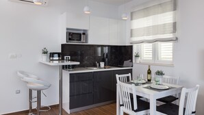 Una cocina moderna con encimera negra, armarios blancos, microondas y una zona de comedor con mesa y sillas blancas.