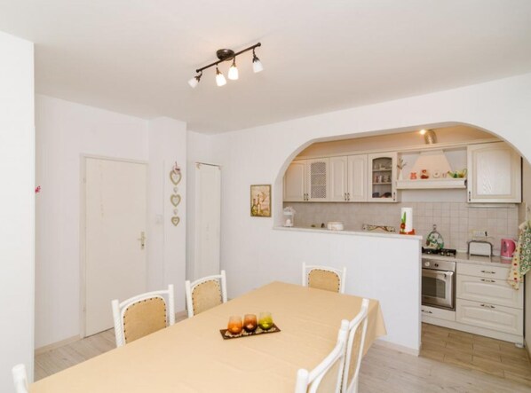 A dining area with a table set for four, a kitchen with white cabinets, and a small oven.