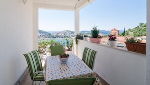 Un balcón con mesa y sillas, plantas en macetas y vistas a un pueblo costero.