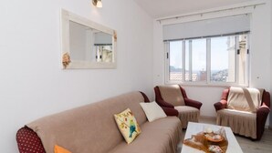 Un salón con un sofá beige, dos sillones, una mesa de centro y un ventanal con vistas a la ciudad.