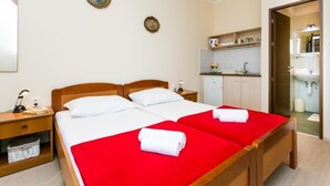 Habitación de hotel con dos camas, un kitchenette pequeño y un baño a la vista a través de una puerta abierta.