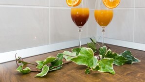 Dos vasos de jugo de naranja con rodajas de naranja sobre una mesa de madera, junto a una planta de hojas variegadas.
