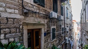 A narrow street with stone buildings, air conditioning units, and a wooden door. - Apartments Minerva - One Bedroom Apartment No.1 (Dubrovnik)