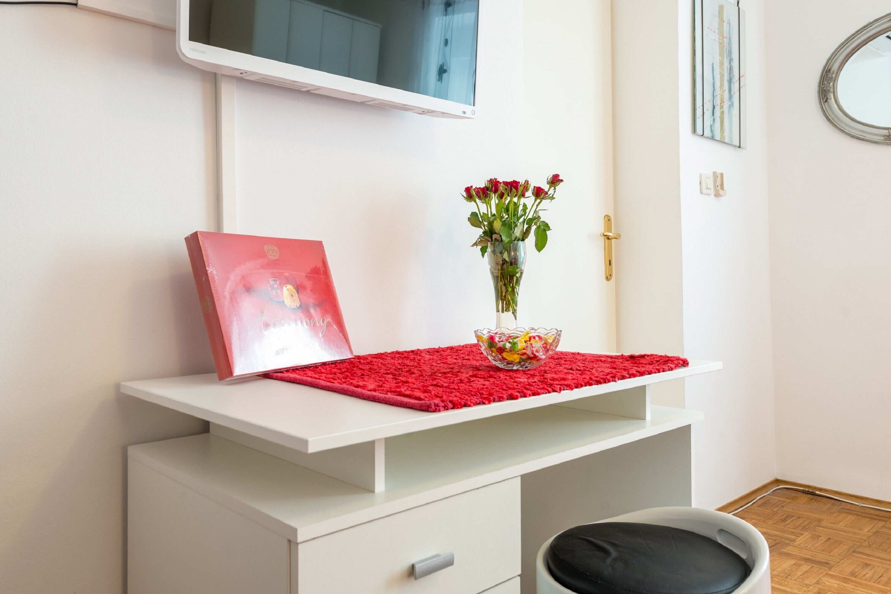 A white desk with a red mat, a vase with red flowers, and a red book.