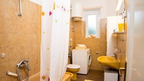 A compact bathroom with a shower, toilet, and washing machine.