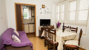 A cozy room with a dining table, chairs, a sofa, a TV, and a window with blinds.