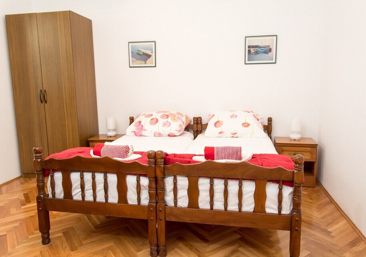 A wooden bed with a red and white bedspread, two bedside tables with lamps, and a wooden wardrobe.