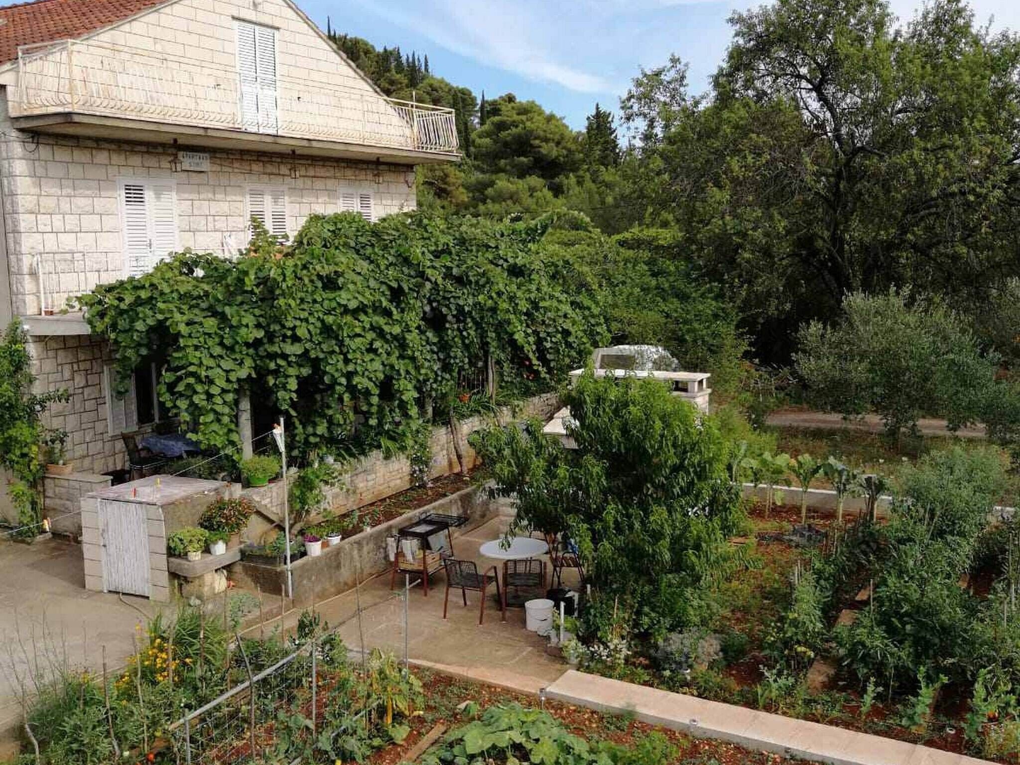 Un bâtiment en pierre doté d’un balcon, entouré d’une végétation luxuriante et agrémenté d’un espace jardin avec des sièges extérieurs.