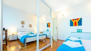 A modern bedroom with a large mirror, a bed with blue bedding, a bedside table, and a small desk with a chair. - Holiday Home Lido - Three Bedroom Holiday House with Terrace (Orebic)