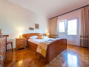 Ein Hotelzimmer mit einem hölzernen Bett, einem Schminktisch, einem Nachttisch und einem Fenster mit Vorhängen.