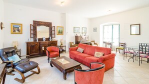 Ein geräumiges Wohnzimmer mit einem roten Sofa, Ledersesseln, einem Couchtisch aus Holz und einem Essbereich mit Glastisch und Stühlen.
