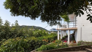 Un edificio moderno de fachada blanca, rodeado de abundante vegetación y vistas a colinas distantes.