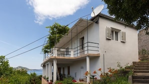Una casa de dos pisos con balcón, antena parabólica y un jardín lleno de flores.