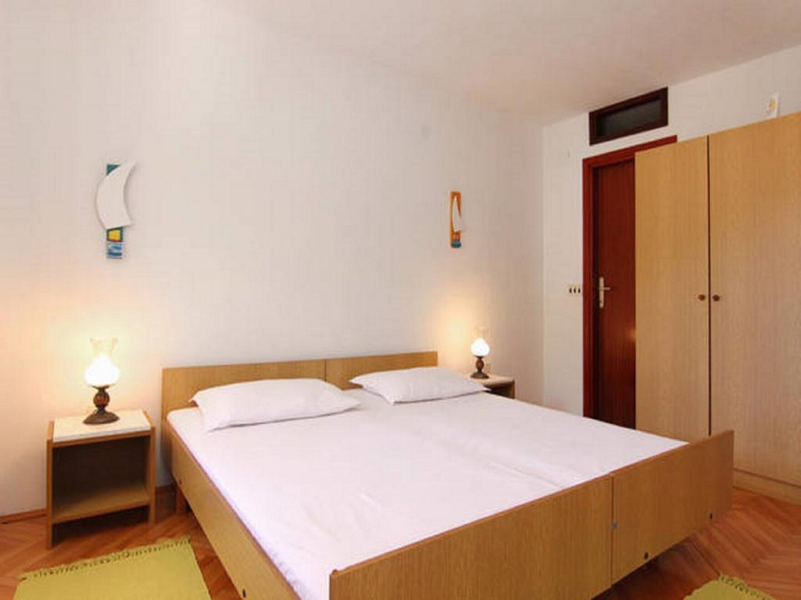 A bedroom with a wooden bed, two bedside tables with lamps, a wardrobe, and a television on the wall.
