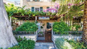 A courtyard with a stone staircase leading to a door, surrounded by lush greenery and flowering plants.