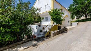 A two-story building with a white facade and yellow trim, a staircase leading to the upper floor, and a small garden area with potted plants. - Villa Bind Comfort Double Room,Patio&Garden ViewR4 (Obod)