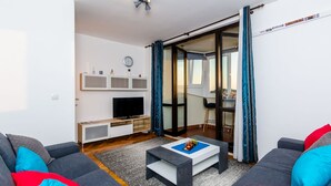 Ein modernes Wohnzimmer mit einer Couch, einem Couchtisch und einem Fernseher. Eine Schiebetür führt zu einem Balkon.